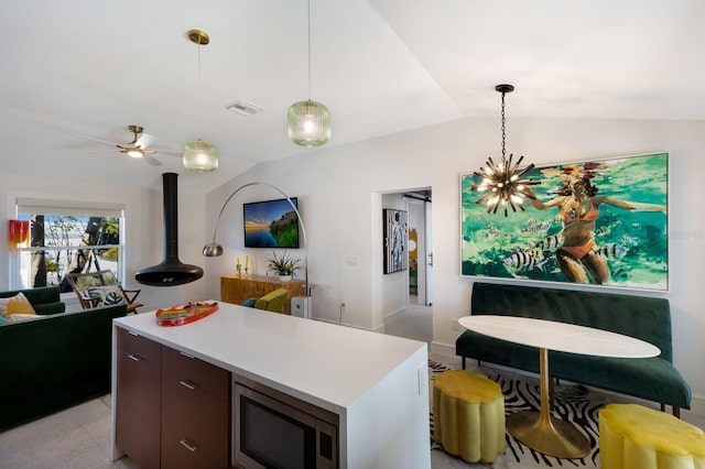 kitchen featuring dark brown cabinetry, decorative light fixtures, a center island, vaulted ceiling, and stainless steel microwave