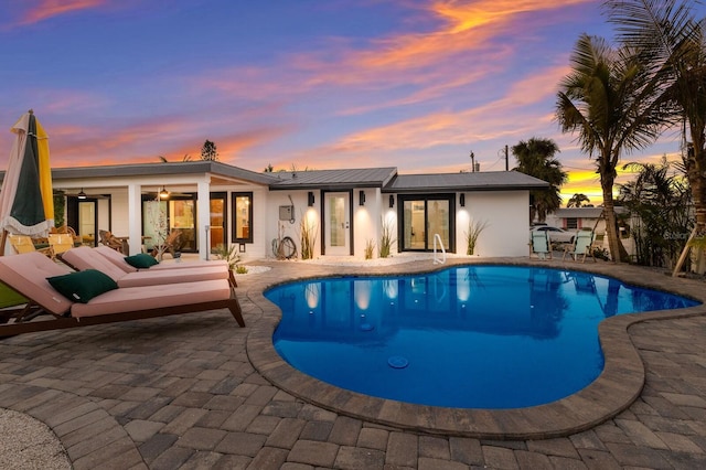 pool at dusk with ceiling fan and a patio area