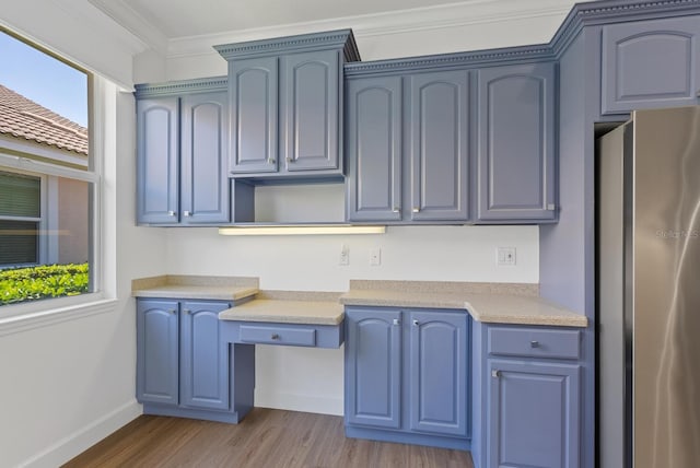 kitchen with blue cabinetry, built in desk, stainless steel refrigerator, ornamental molding, and light hardwood / wood-style floors