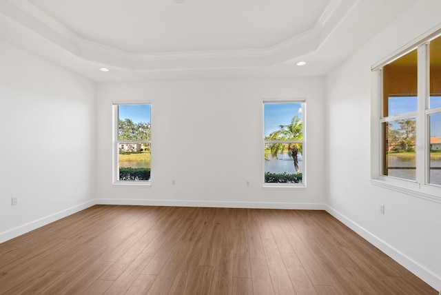 empty room with a raised ceiling, ornamental molding, a water view, and hardwood / wood-style floors