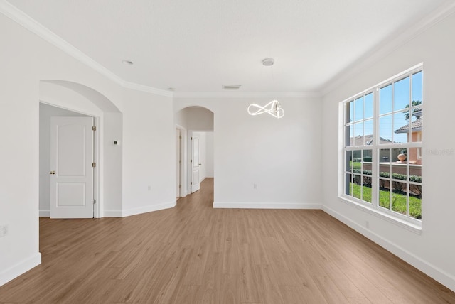 spare room with arched walkways, visible vents, ornamental molding, light wood-type flooring, and baseboards