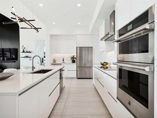 kitchen featuring sink, wall chimney range hood, appliances with stainless steel finishes, white cabinets, and light tile patterned flooring