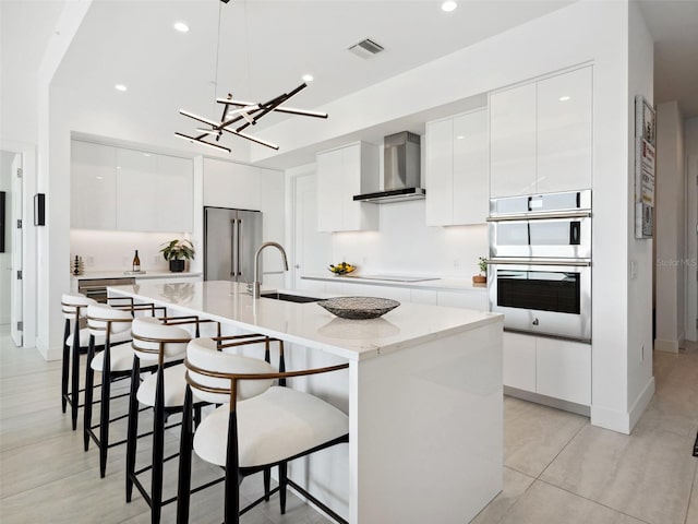 kitchen with an island with sink, stainless steel appliances, sink, and wall chimney range hood