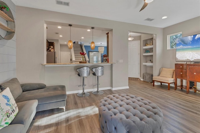 living room featuring wood-type flooring, built in features, and ceiling fan