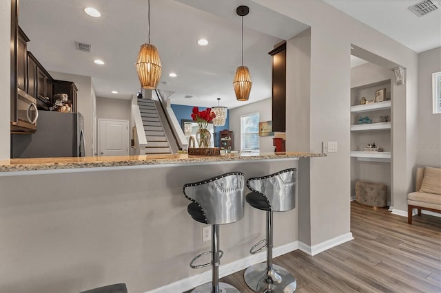 kitchen featuring stainless steel appliances, decorative light fixtures, kitchen peninsula, and built in features