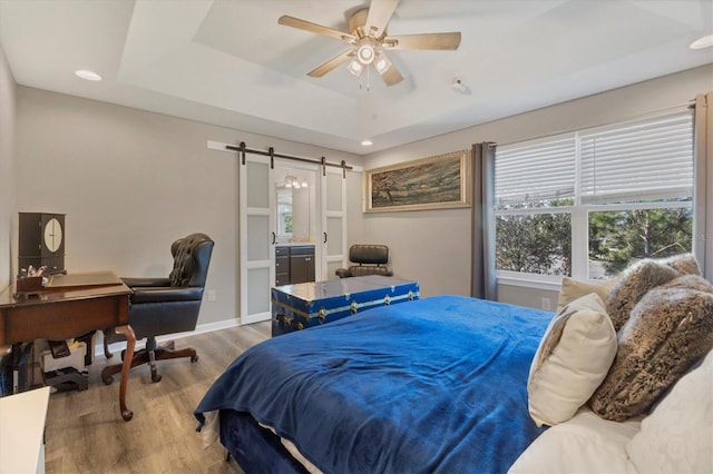 bedroom with wood-type flooring, a barn door, ceiling fan, and a tray ceiling