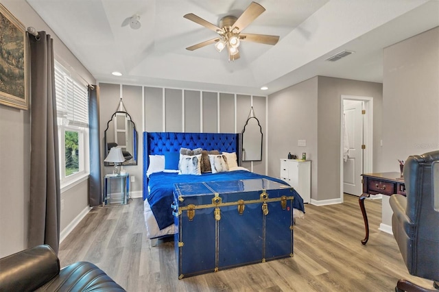 bedroom with ceiling fan, a tray ceiling, and light hardwood / wood-style floors