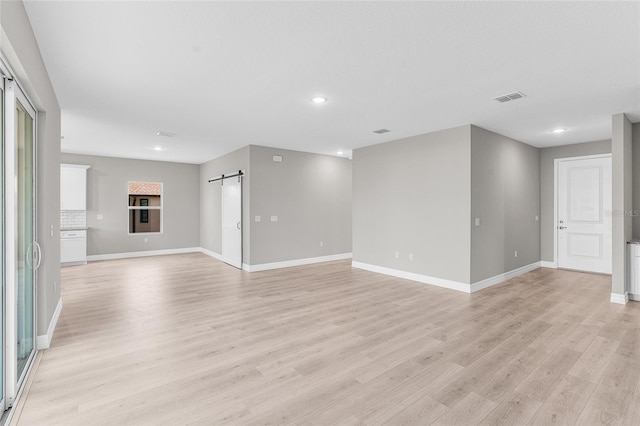 unfurnished living room featuring a barn door and light wood-type flooring