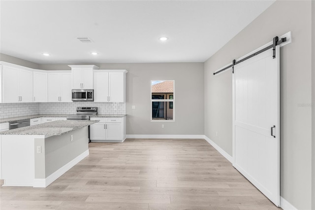 kitchen featuring white cabinetry, light wood-type flooring, stainless steel appliances, a barn door, and light stone countertops