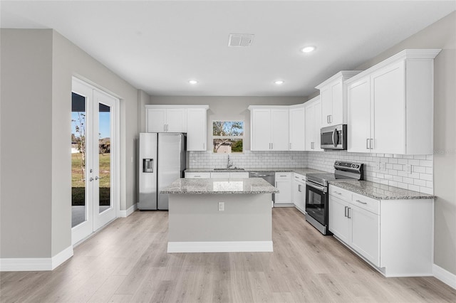 kitchen featuring light stone countertops, stainless steel appliances, a center island, and white cabinets