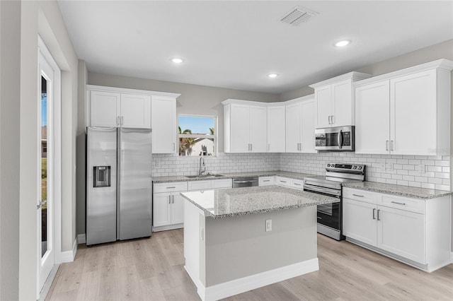 kitchen featuring sink, white cabinets, a center island, stainless steel appliances, and light stone countertops