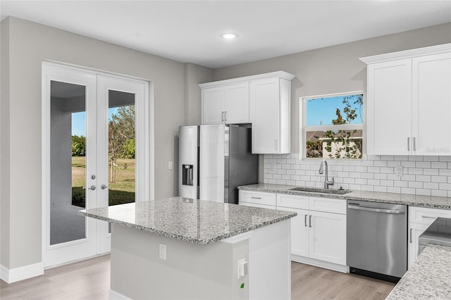 kitchen with sink, white cabinetry, stainless steel appliances, light stone countertops, and a kitchen island