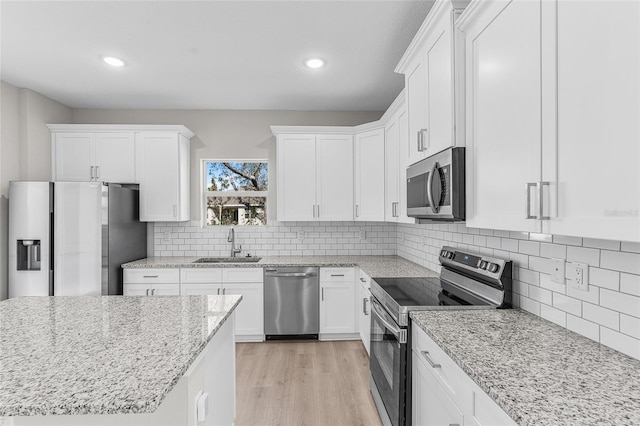 kitchen featuring appliances with stainless steel finishes, white cabinetry, sink, light stone countertops, and light wood-type flooring