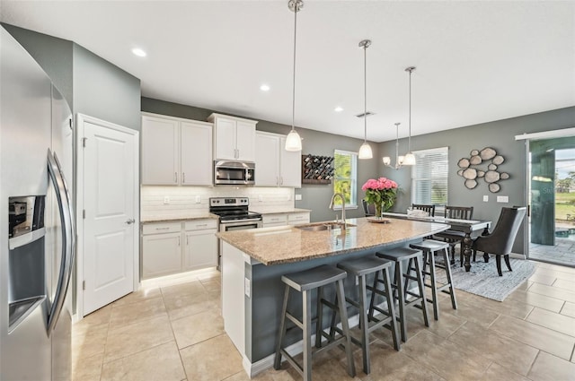 kitchen with a center island with sink, a sink, tasteful backsplash, appliances with stainless steel finishes, and light stone countertops