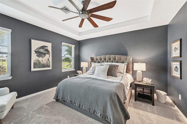 carpeted bedroom featuring a ceiling fan, a raised ceiling, and baseboards