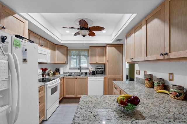 kitchen with light brown cabinetry, sink, a tray ceiling, white appliances, and light stone countertops