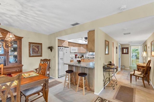 kitchen with light tile patterned floors, white appliances, sink, light stone countertops, and a kitchen bar