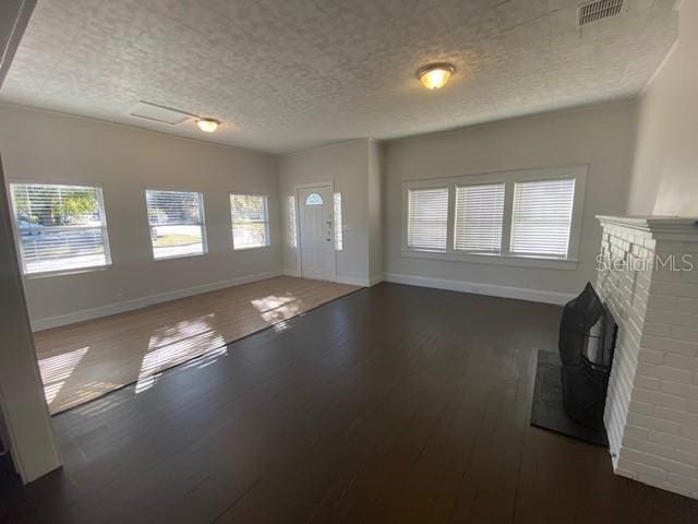 unfurnished living room with a brick fireplace, dark wood-type flooring, and a textured ceiling