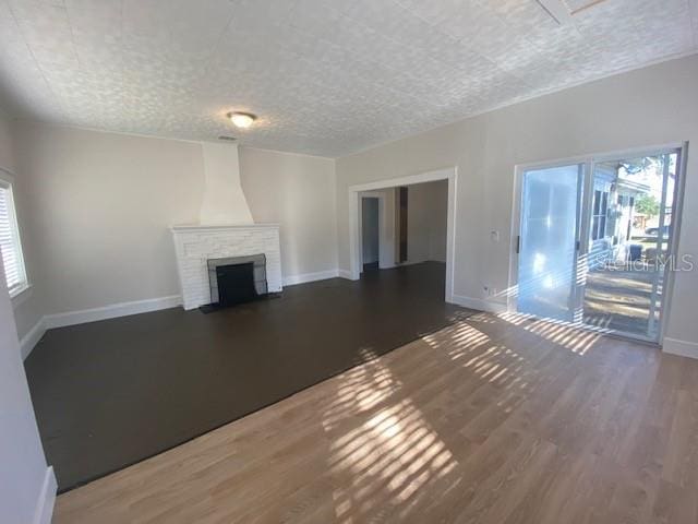 unfurnished living room featuring a brick fireplace, a wealth of natural light, a textured ceiling, and dark hardwood / wood-style flooring