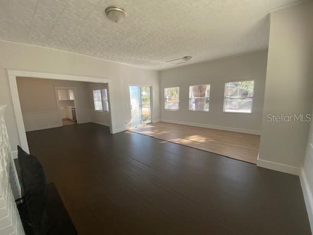 unfurnished living room featuring plenty of natural light, a textured ceiling, and dark hardwood / wood-style flooring