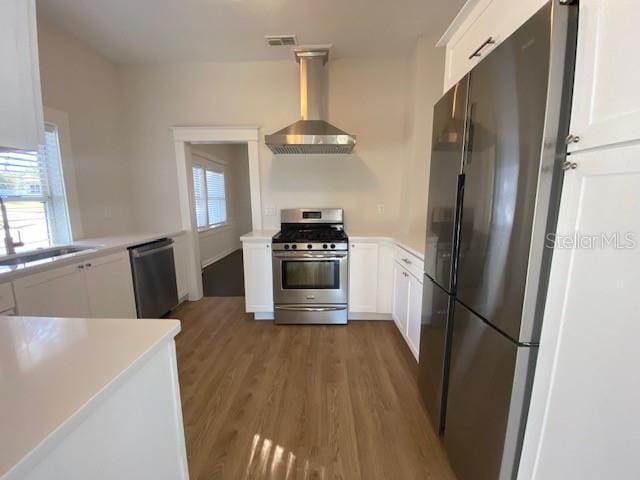 kitchen featuring wall chimney range hood, sink, stainless steel appliances, a healthy amount of sunlight, and white cabinets