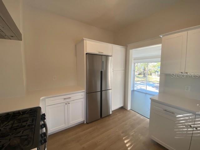 kitchen featuring light hardwood / wood-style flooring, stainless steel refrigerator, range with gas stovetop, white cabinets, and exhaust hood