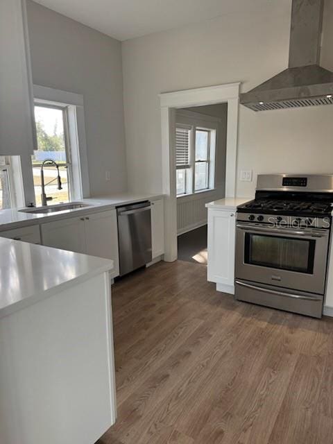 kitchen with wall chimney exhaust hood, sink, appliances with stainless steel finishes, hardwood / wood-style flooring, and white cabinets