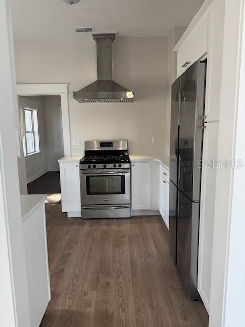 kitchen with black refrigerator, white cabinets, stainless steel range with gas stovetop, and wall chimney exhaust hood