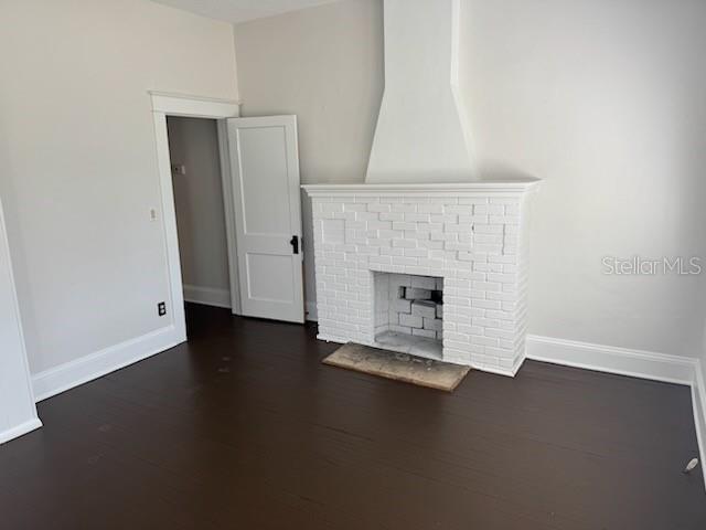 unfurnished living room with a brick fireplace and dark wood-type flooring