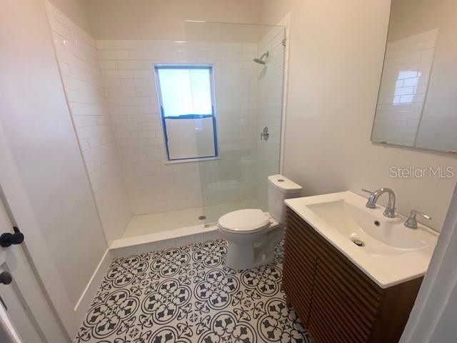 bathroom with a tile shower, vanity, tile patterned flooring, and toilet