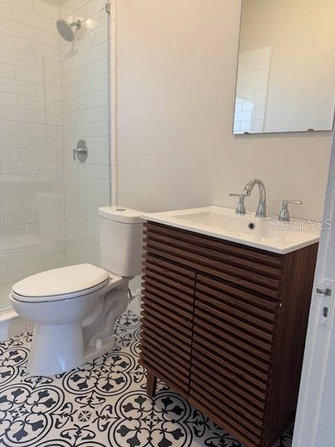 bathroom with vanity, tile patterned floors, toilet, and a tile shower