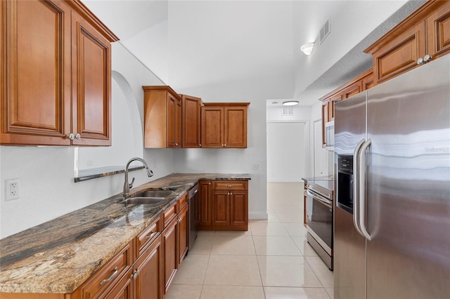 kitchen featuring appliances with stainless steel finishes, a towering ceiling, sink, dark stone counters, and light tile patterned floors