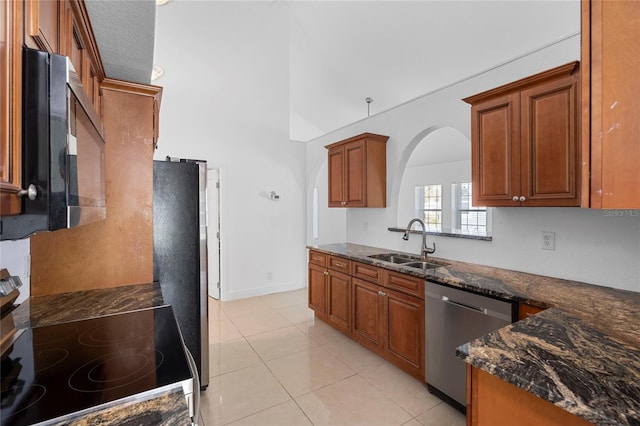 kitchen featuring stainless steel appliances, sink, light tile patterned floors, and dark stone counters