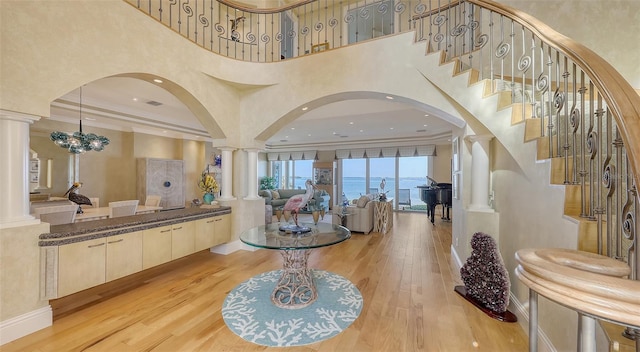 foyer entrance with decorative columns, a water view, ornamental molding, a notable chandelier, and light hardwood / wood-style floors