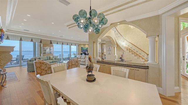 dining room with ornate columns, ornamental molding, a water view, and light hardwood / wood-style flooring