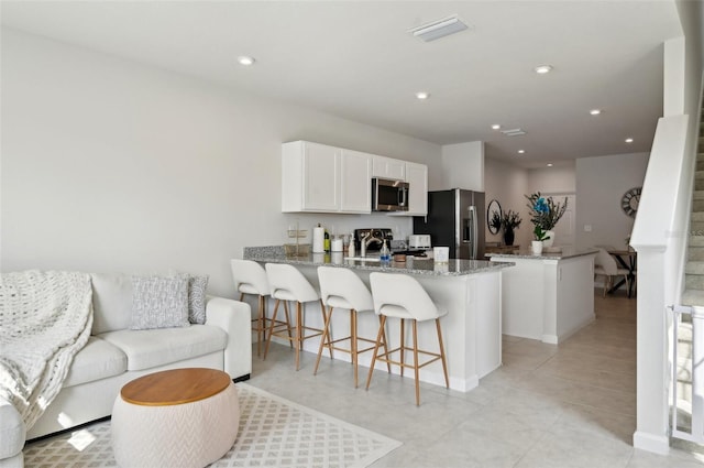 kitchen with a kitchen breakfast bar, kitchen peninsula, stainless steel appliances, light stone countertops, and white cabinets