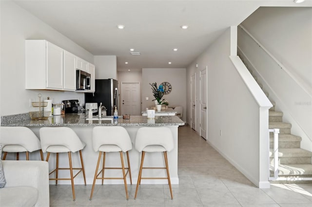 kitchen featuring a breakfast bar area, white cabinetry, stone countertops, appliances with stainless steel finishes, and kitchen peninsula