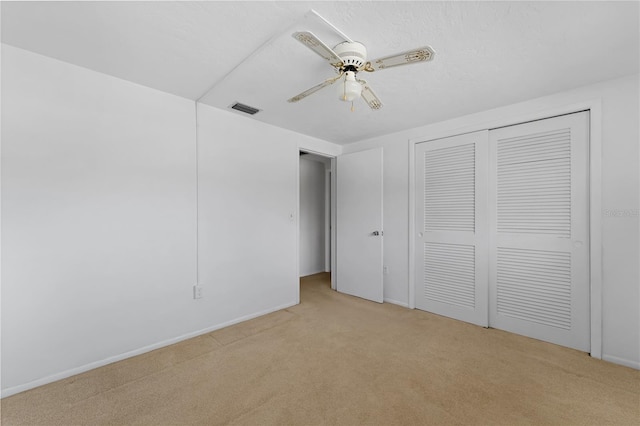 unfurnished bedroom featuring light carpet, a textured ceiling, ceiling fan, and a closet