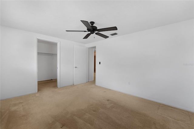 unfurnished bedroom featuring light carpet, a spacious closet, a closet, and ceiling fan