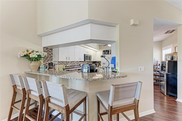 kitchen featuring stainless steel appliances, light stone countertops, white cabinets, and kitchen peninsula