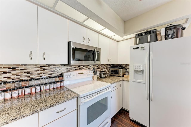 kitchen featuring tasteful backsplash, light stone countertops, white cabinets, and white appliances