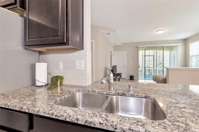 kitchen with tasteful backsplash, light stone countertops, sink, and dark brown cabinetry