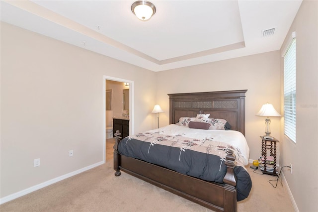 carpeted bedroom with multiple windows, ensuite bathroom, and a tray ceiling