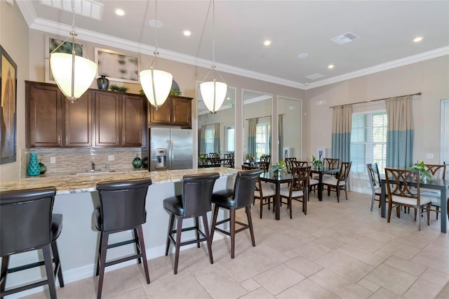 kitchen featuring ornamental molding, decorative light fixtures, stainless steel fridge with ice dispenser, and a breakfast bar area