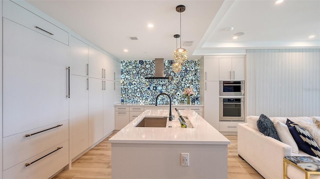 kitchen featuring a center island with sink, wall chimney range hood, sink, and pendant lighting