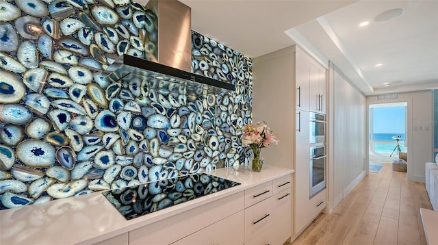 kitchen with white cabinets, a water view, black cooktop, light wood-type flooring, and wall chimney exhaust hood