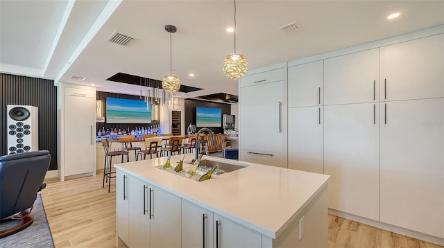 kitchen featuring pendant lighting, white cabinetry, an island with sink, sink, and light hardwood / wood-style floors