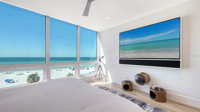 unfurnished bedroom featuring hardwood / wood-style floors, ceiling fan, a beach view, and a water view