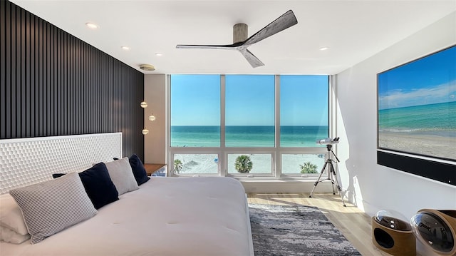 bedroom with a water view, ceiling fan, a beach view, and light hardwood / wood-style flooring