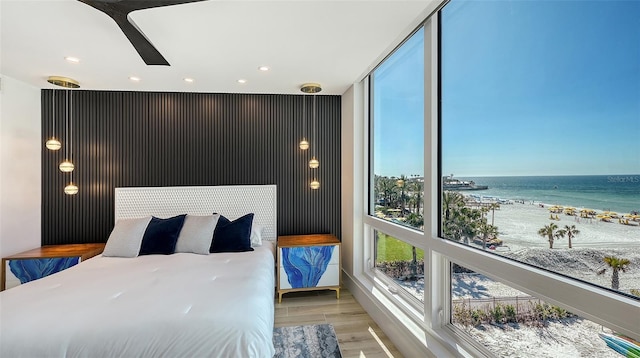 bedroom with a water view, floor to ceiling windows, a view of the beach, and hardwood / wood-style floors